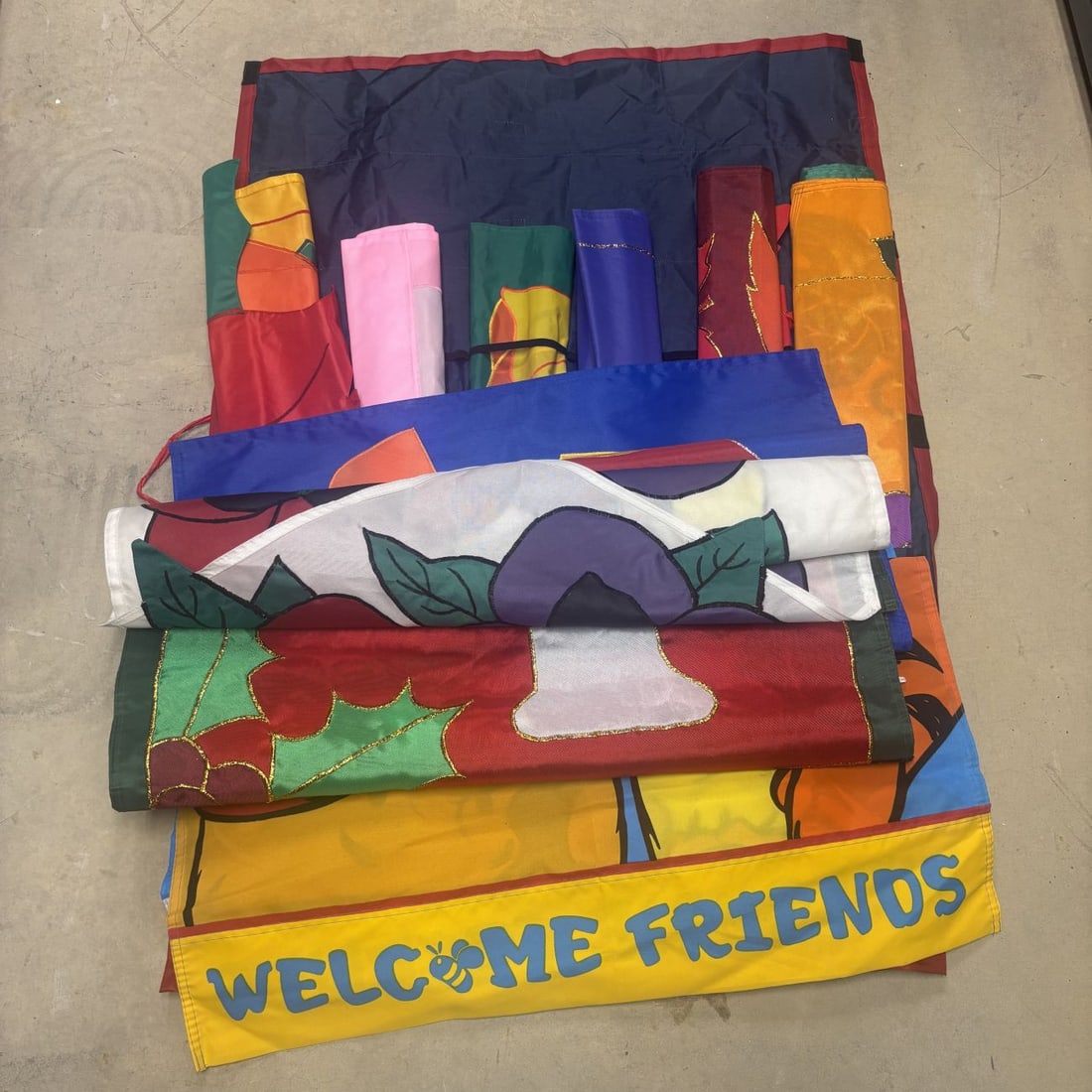 An Assortment of Seasonal Appliqued and Embroidered Decorative House Flags with Storage Organizer: A collection of outdoor decorative flags crafted from synthetic fabric featuring various seasonal and holiday motifs. The flags utilize a combination of appliqued fabric layers and embroidered detaili