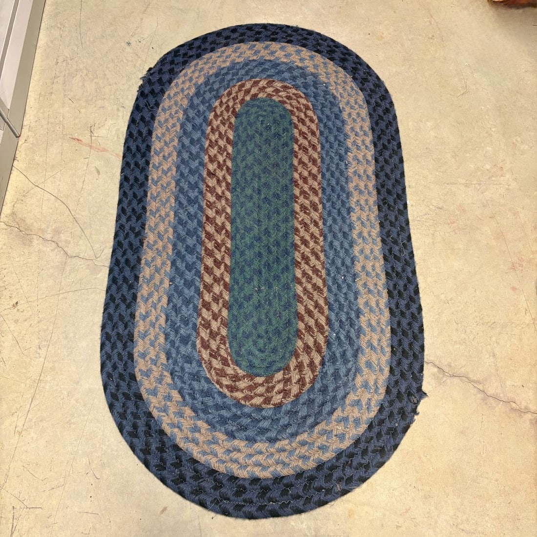 Traditional Oval Multi-Color Braided Floor Rug: A traditional oval braided floor rug featuring concentric bands of flat-braided textile material. The design center is a teal green oval surrounded by bands of reddish-brown and tan, medium blue, a li