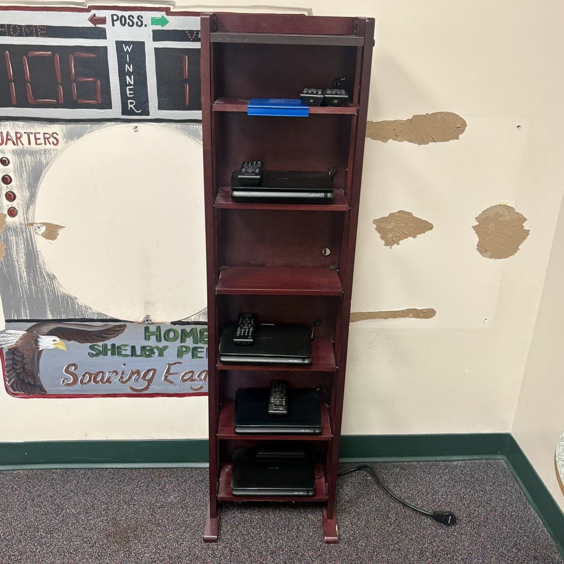 A Wooden Six-Tier Media Shelf and a Collection of Sony Portable DVD Players: This lot comprises a tall, narrow six-tier vertical storage shelf and a collection of portable electronics. The shelf is constructed of wood with a dark reddish-brown mahogany-style finish and