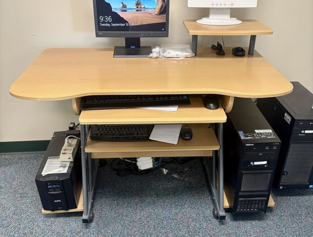 Multi-Tier Mobile Computer Workstation with Lenovo ThinkServer and Assorted Computer Hardware: This mobile multi-tier computer workstation features light oak-effect laminate surfaces on a gray metal frame supported by four swiveling casters. The desk includes a contoured main work surface, a ra
