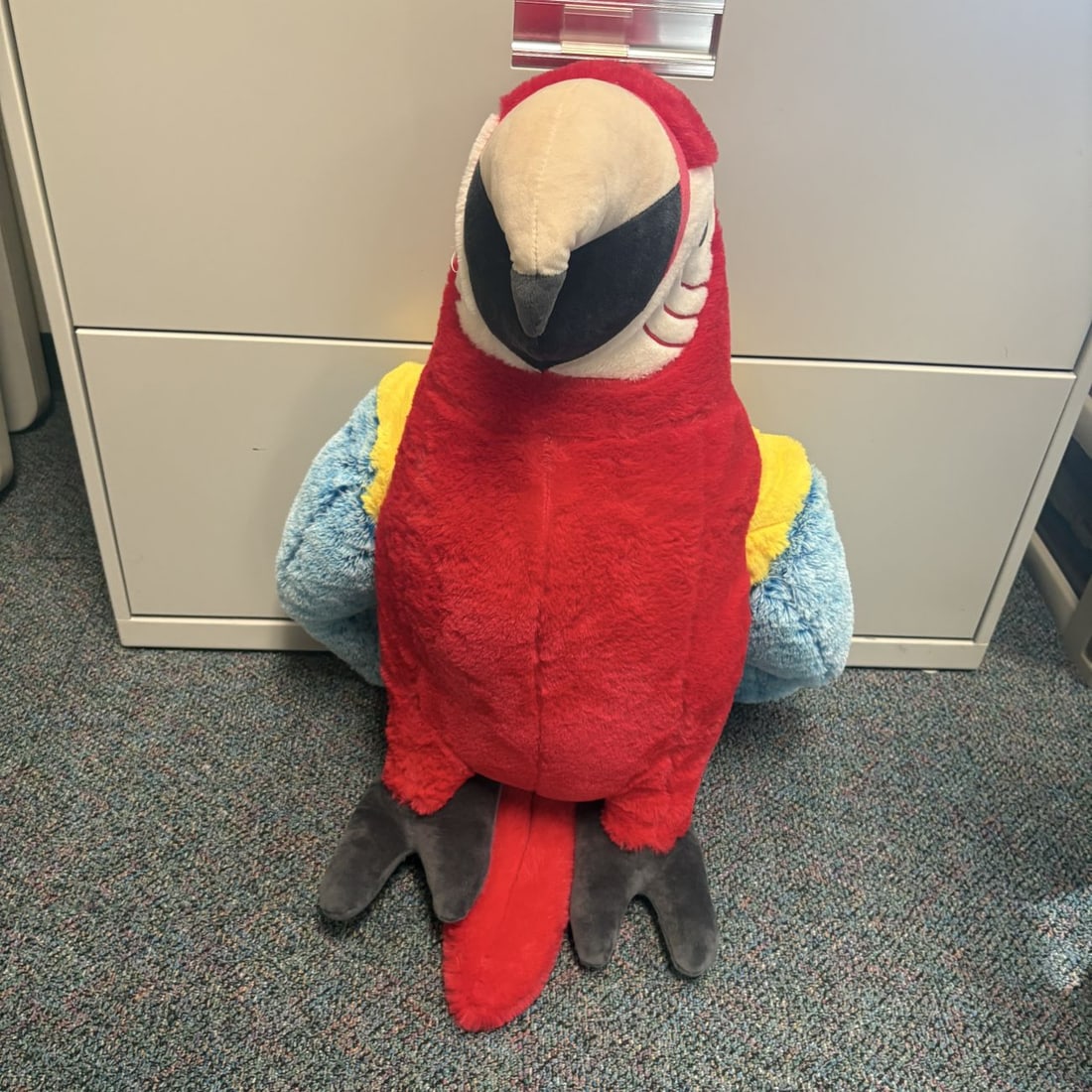 Large Scarlet Macaw Plush Stuffed Animal Toy: An oversized plush toy representing a scarlet macaw parrot, constructed in a seated position. The toy is made from multi-colored synthetic plush fabric in shades of red, white, yellow, and light