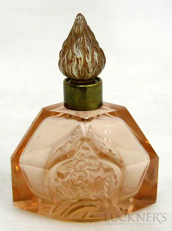 An Art Deco Perfume Bottle: Of translucent salmon-coloured cut glass, with a brass collar and painted, pressed glass stopper. Features a central frosted glass panel with a floral motif. First half 20th century. H. 11.7 cm (4.7 i