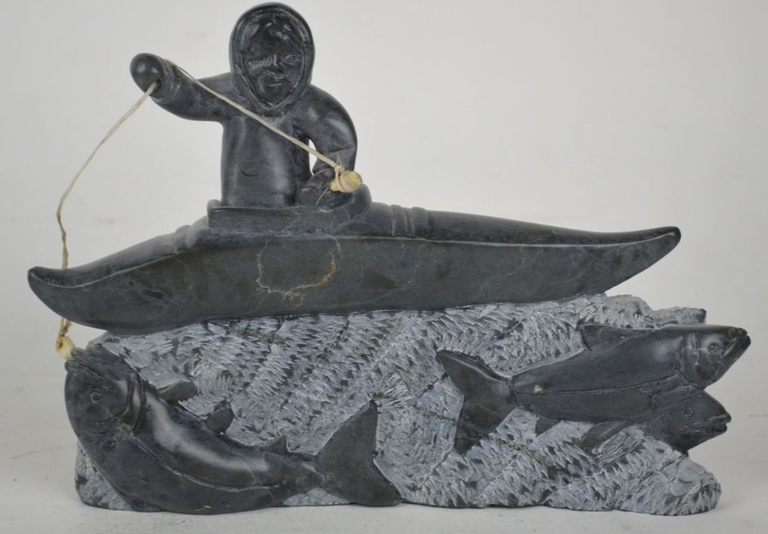 JIMMY ARNAMISSAK STONE INUIT SCULPTURE SIGNED: Jimmy Inaruli Arnamissak (Inuit / Inukjuak B. 1946). A very good carved stone (with bone elements, e.g. hook) sculpture of a hunter / fisher in a kayak pulling salmon. The work is signed/ incised to b