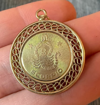 Vintage 14K Gold Scorpio Zodiac Charm (S): Circular zodiac medallion with a high-relief textured scorpion figure over a polished 14K yellow gold background. Diamond-cut border detailing. Diameter: 16 mm (22 mm total drop with bale). Weight: 1.