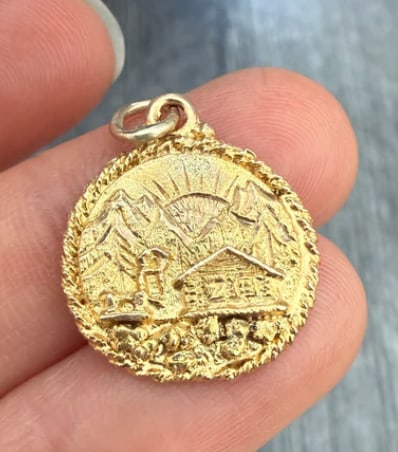 Vintage Alaska Gold Rush Mountain Scenery Charm in 10K Gold: Intricate scenic pictorial travel disk portraying a hand-carved Alaskan wilderness mountain vista complete with cabin, pine trees, and a riverbed overlaid with raw gold nugget flakes. Medallion diamet