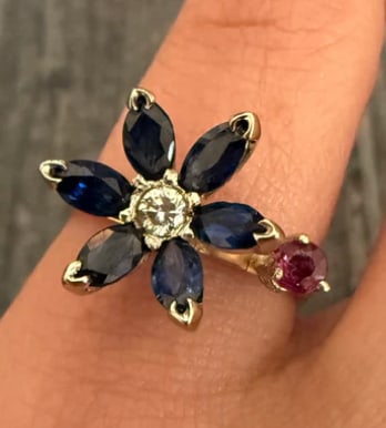 Sapphire Flower, Ruby and 14K Gold Ring (S): Dainty feminine cluster ring stacking a central natural red ruby cabochon surrounded by a crown ring of 6 petite round navy-blue sapphires forming a floral daisy head layout. Slim polished gold shank.