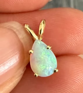 Teardrop Pear Shaped Opal Solitaire Charm: Minimalist gemstone drop pendant holding a fiery pear-cut natural white opal cabochon within a clean three-prong setting. Strong flashes of multi-colored red and green play. Drop length: 14 mm includi
