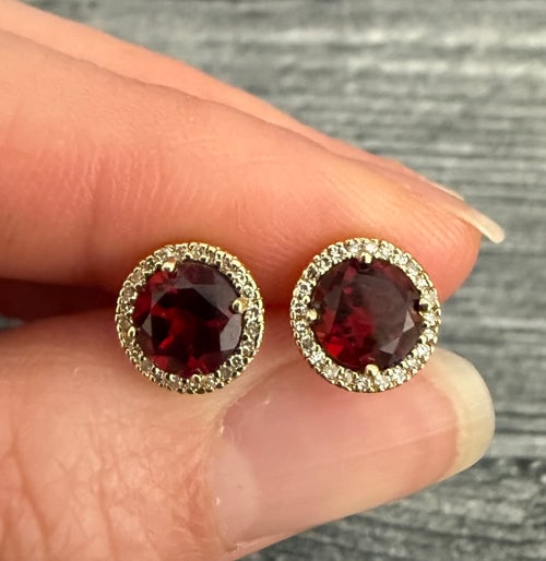 Garnet and Diamond Halo Stud Earrings: Elegant 14K yellow gold stud earrings featuring vibrant round-cut garnets surrounded by a delicate halo of shimmering diamonds.