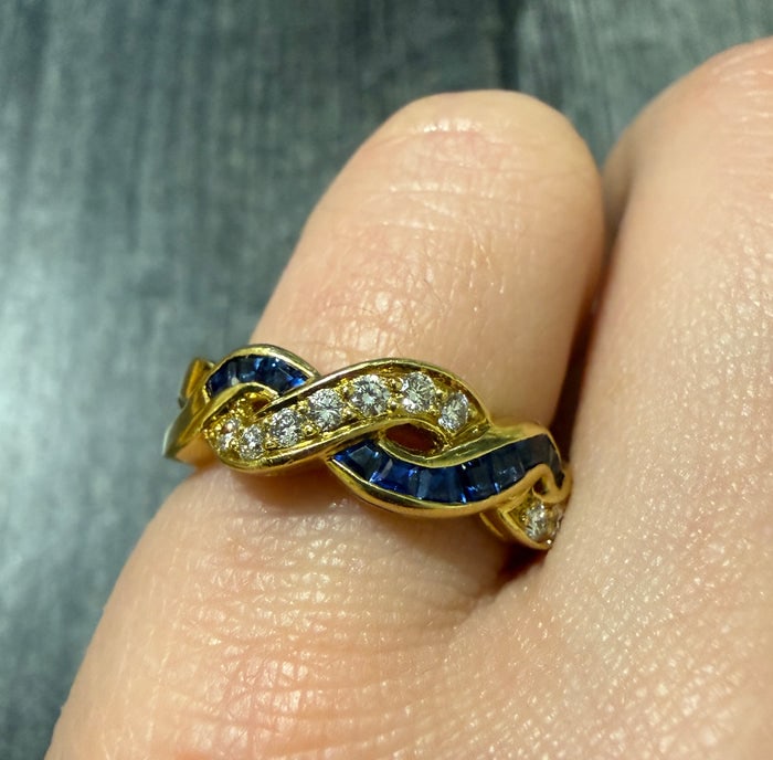 Sapphire and Diamond Twist Band in 18K Gold: A dynamic 18K gold band featuring a twisted design set with blue sapphires and brilliant diamonds.