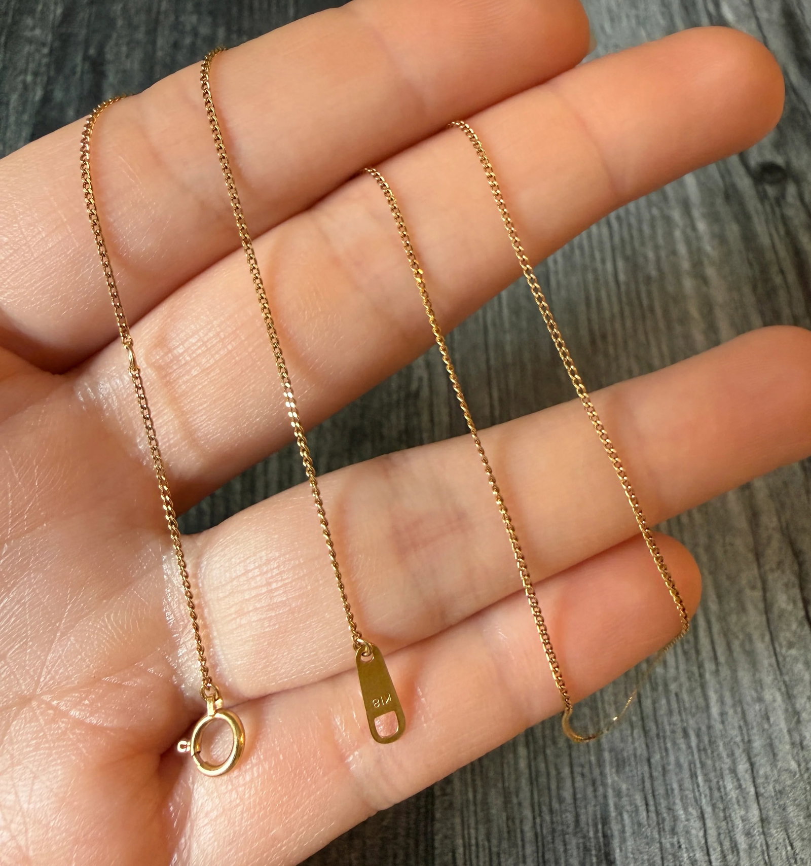 Thin 18K Gold Curb Link Chain, 15.25?? Long (S): Metal: 18K Yellow Gold Weight: 1.6 gramsMeasurements: Adjustable length of 15.25 inches to 14.25 inches long by 0.8 mm wideMarkings: "K18"Condition: In very good condition with some minor surface wear
