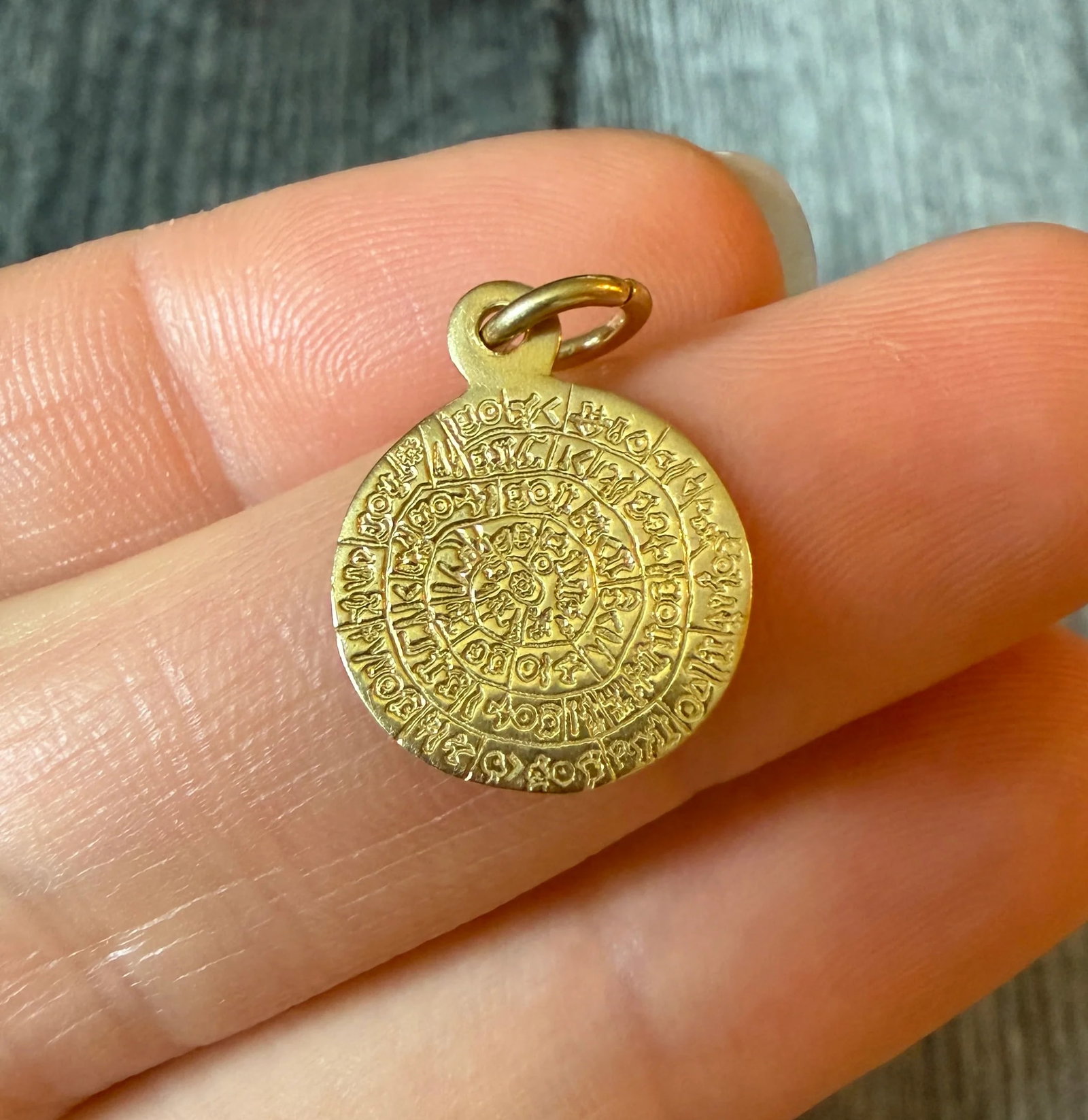 Greek Phaistos Disc Charm in 14K Gold: Metal: 14K Yellow Gold Weight: 1.6 gramsMeasurements: 0.55 inch diameter Condition: In very good condition with some minor surface wear Follow us on Instagram @alphaomegajewelry for the latest updates