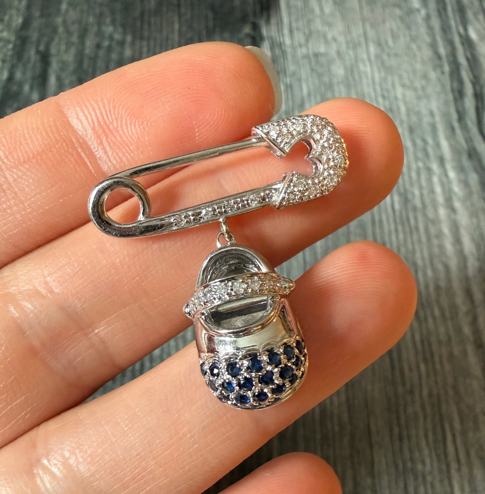 Diamond and Sapphire Safety Pin with a Dangling Shoe Charm (S): Metal: 14K White Gold Weight: 6.3 gramsMeasurement: 1.2 inches long by 1.15 inches wideDiamonds: Approximately 0.09 caratsSapphires: Approximately 0.70 carats Markings: "14K 585" and an inscription Co