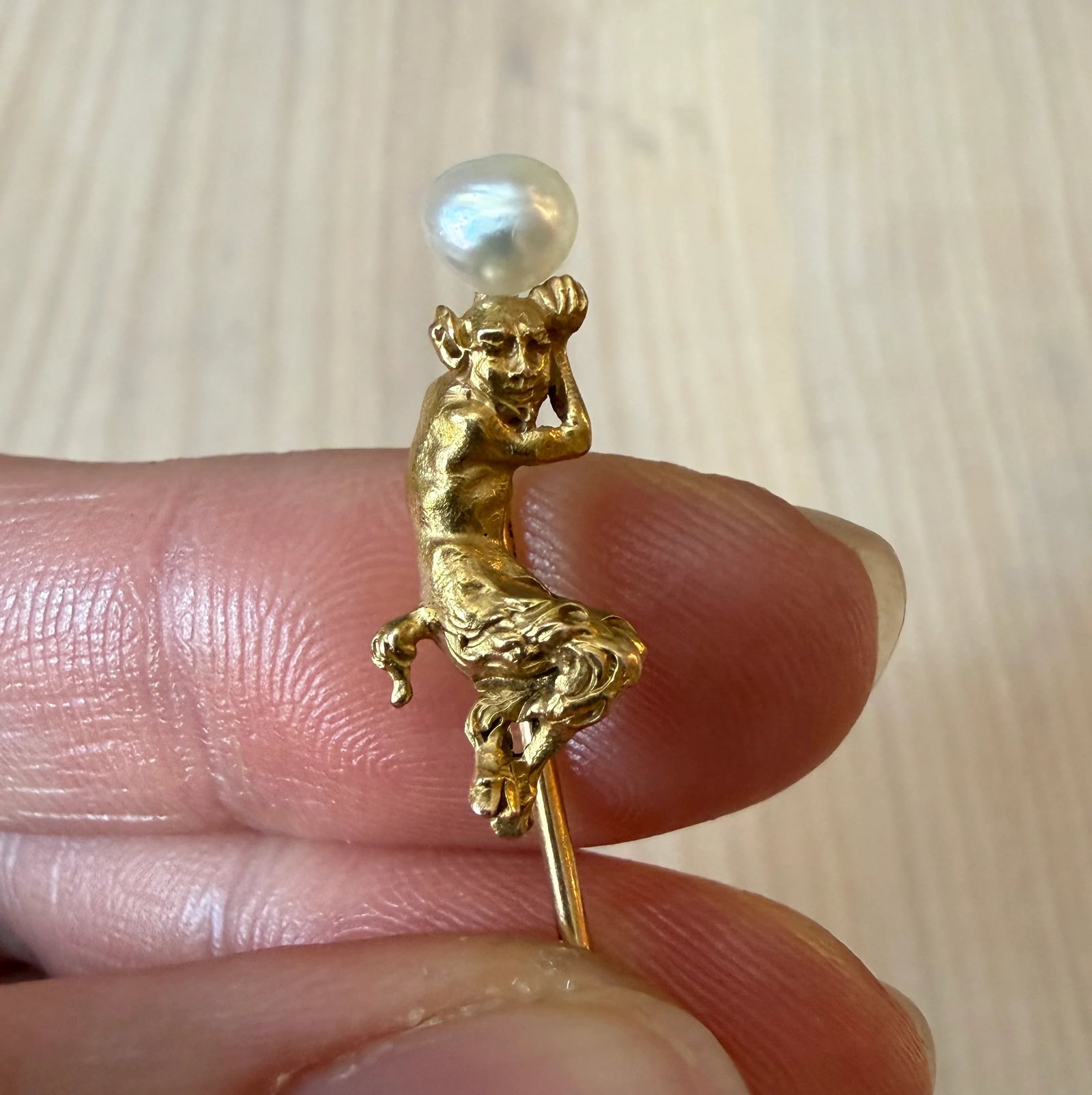 Art Nouveau Figural Faun or Satyr Stick Pin: A highly detailed Art Nouveau era stick pin of a faun or satyr with fur-textured lower legs holding a pearl above its head.Metal: 14K Yellow GoldWeight: 2.8 gramsFaun Measurements: 0.8" long by 0.35"