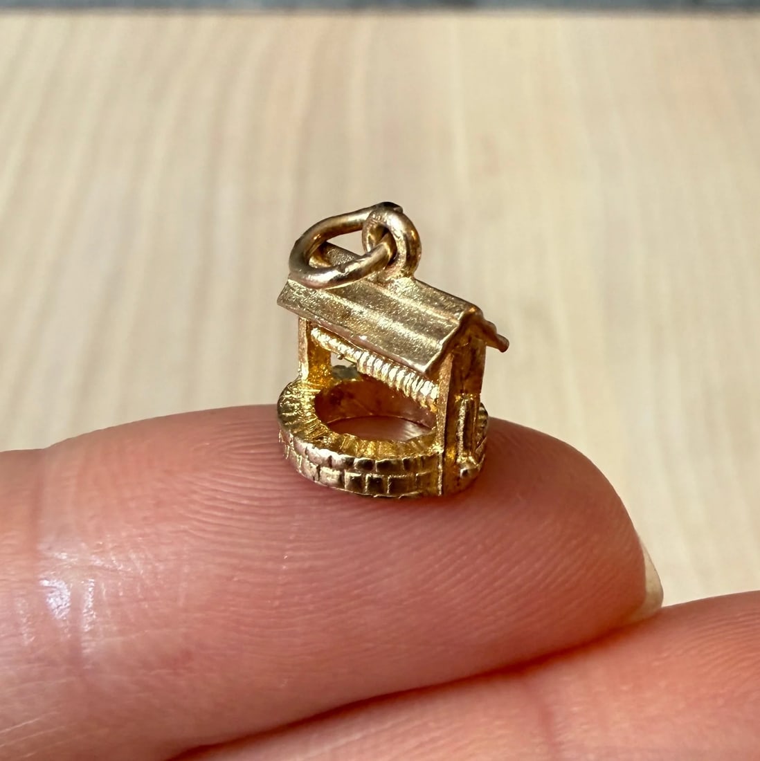 Small Midcentury English Wishing Well Charm in 9K Gold: A small three dimensional wishing well charm with a brick-textured base, a small gabled roof, and a mini pitcher. The bottom of the charm is stamped with full English assay marks.Metal: 9K Yellow Gold