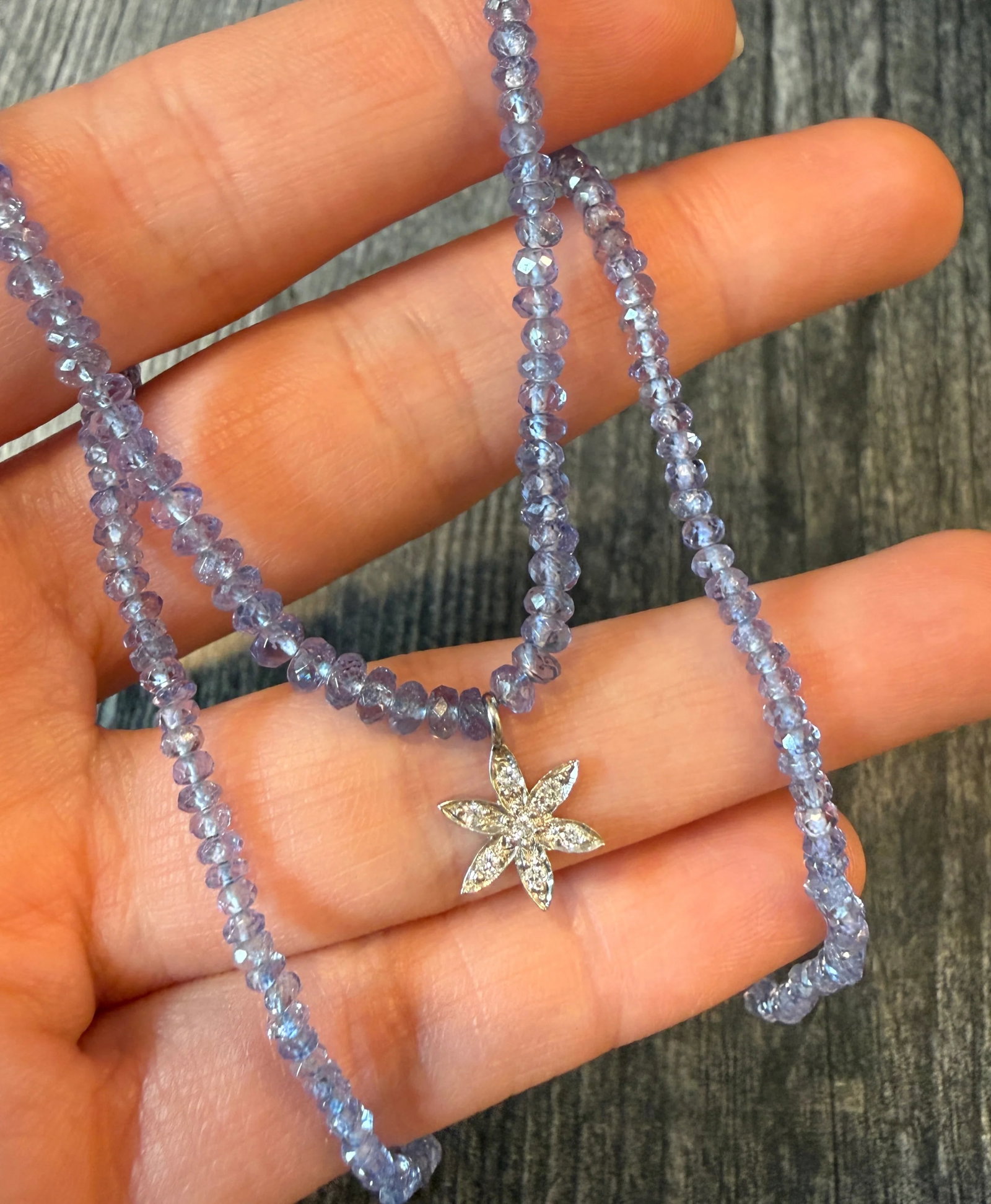 Tanzanite Bead Necklace with a Diamond Flower Charm: Metal: 18K White Gold Weight: 7.9 gramsDiamonds: Approximately 0.11 caratsNecklace Measurements: 15.5 inches long by 3.2 mm wide beadsMarkings: "750"Condition: In good condition with some minor surfac