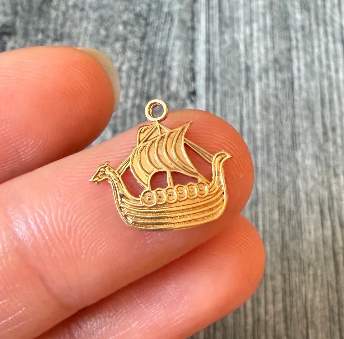 Small Viking Ship Charm in 14K Gold: Metal: 14K Yellow GoldWeight: 0.7 gramsMeasurements: 0.5 inches long by 0.55 inches wideMarkings: "SVERIGE"Condition: In very good condition with some minor surface wear. A bale can be added if reques