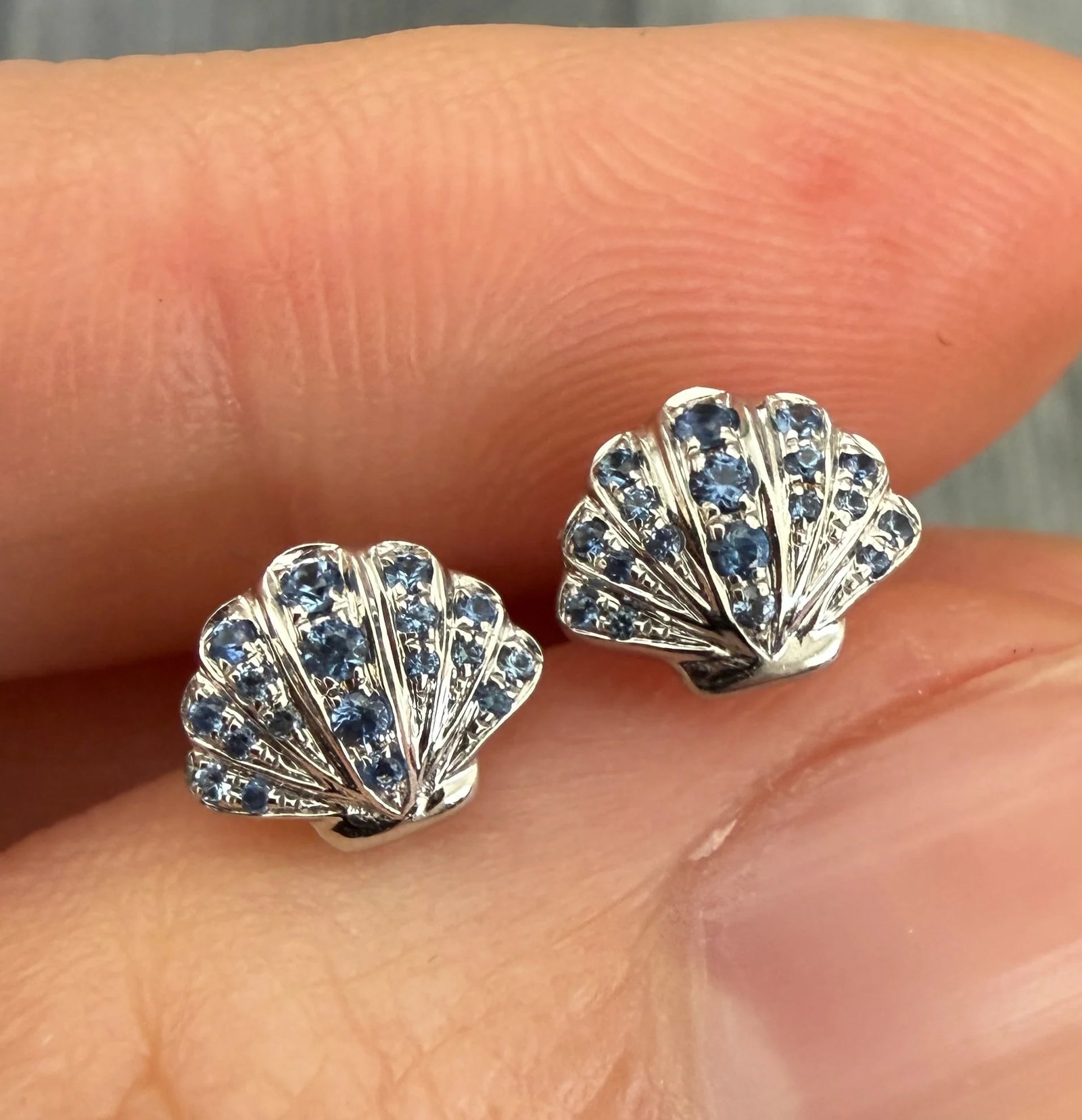 Sapphire and 18K White Gold Seashell Stud Earrings: Metal: 18K White GoldWeight: 2.4 gramsSapphires: Approximately 0.32 caratsMeasurements: 0.25 inches long by 0.35 inches wideMarkings: "750"Condition: In very good condition with only minor surface