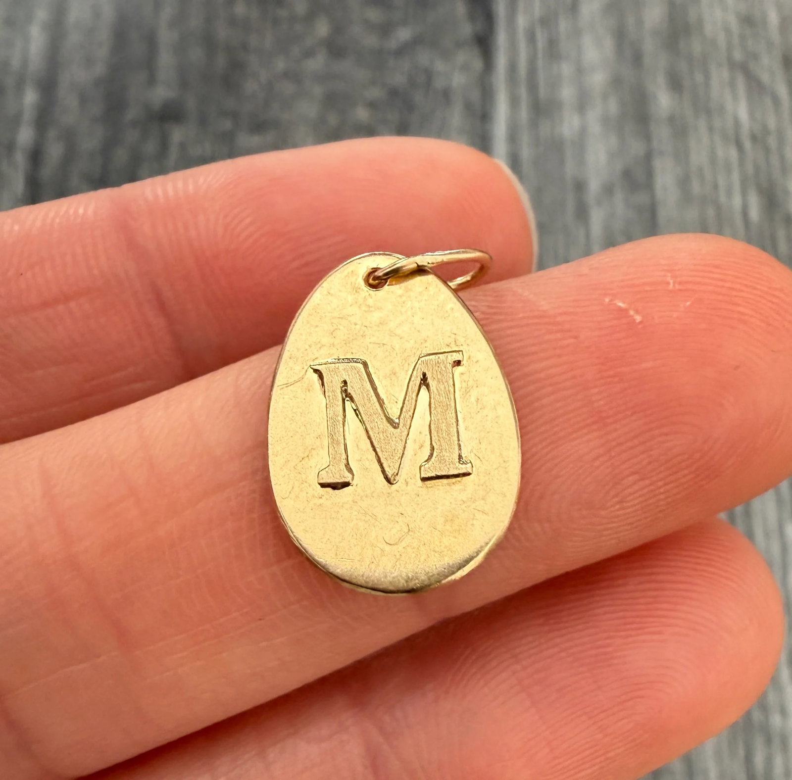 Vintage Egg Shaped Initial M Charm in 18K Gold: Metal: 18K Yellow Gold (acid tested)Weight: 0.9 gramsMeasurements: 0.7 inches long by 0.5 inches wideMarkings: NoneCondition: In good condition with some minor surface wearFollow us on Instagram @alph