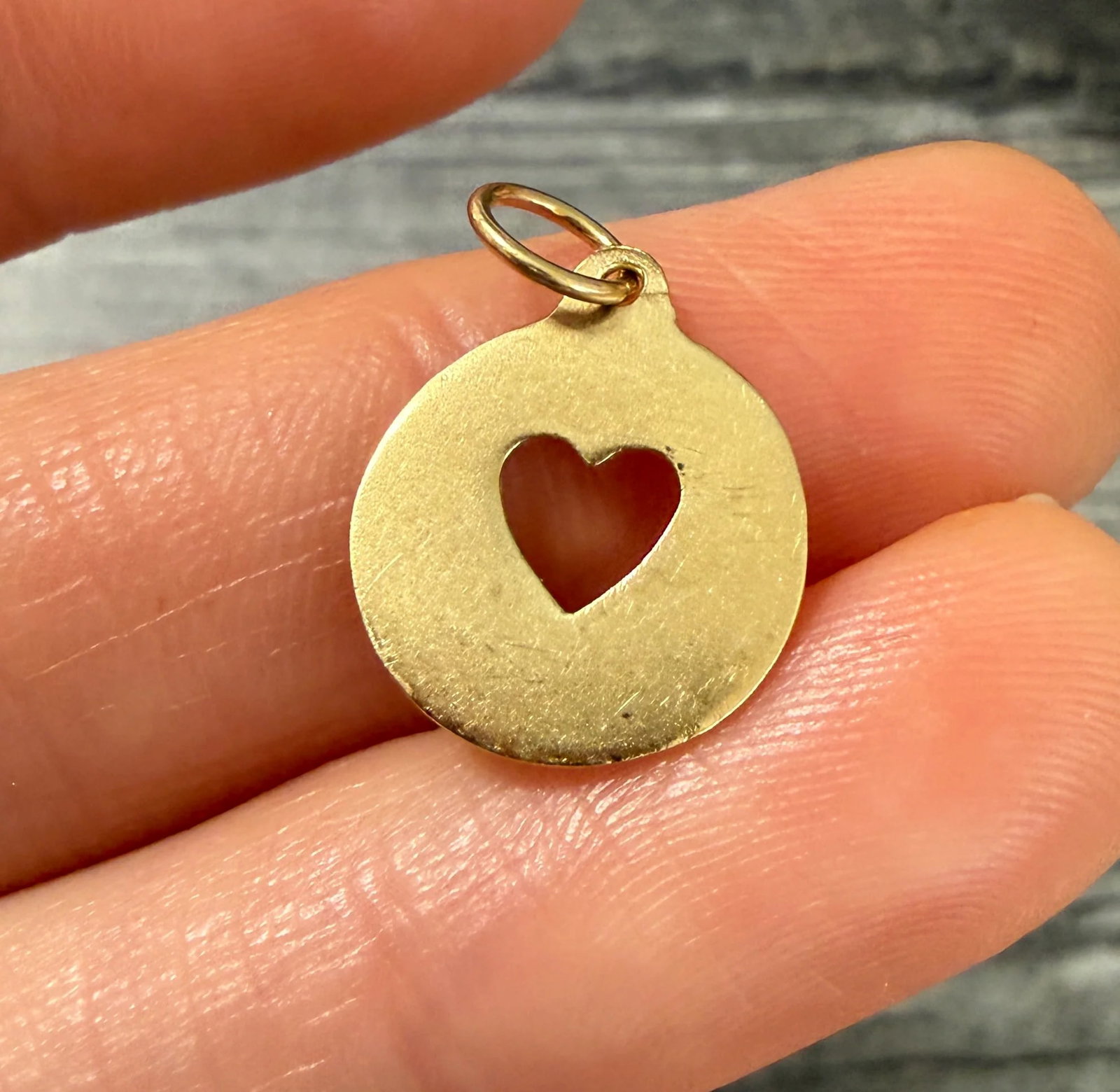 14K Gold Cut Out Heart Disc Charm: Metal: 14K Yellow Gold Weight: 1.4 gramsMeasurements: 0.55 inches diameter Markings: "14K"Condition: In good condition with some minor surface wear.Follow us on Instagram @alphaomegajewelry for the la