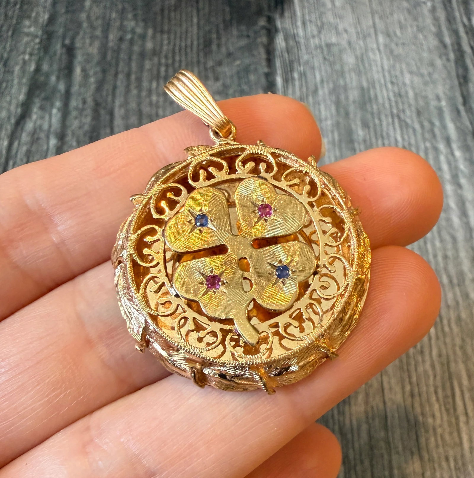 Large Vintage Ruby and Sapphire Clover Charm with Scrolled Border in 14K Gold: Metal: 14K Yellow Gold Weight: 11.9 gramsMeasurements: 1.3 inch diameter Inscribed: "Happy 10th Anniversary Love From the Three Of Us" Condition: In m good condition with some minor surface wear.Follo