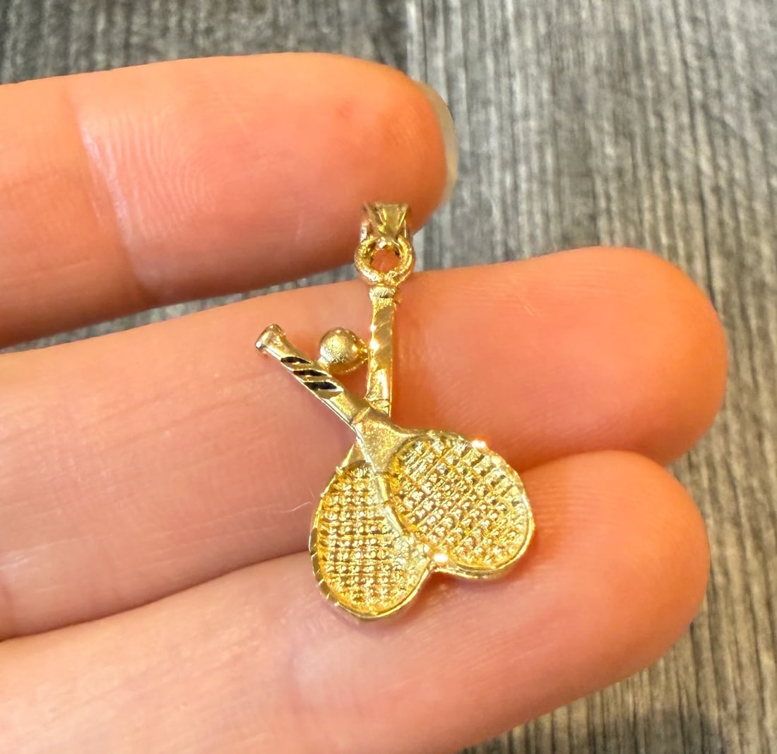 Tennis Rackets and Ball Charm in 14K Gold: Metal: 14K Yellow Gold Weight: 1.5 gramsMeasurements: 0.7 inches long by 0.5 inches wideMarkings: "14K"Condition: In very good condition with some minor surface wear.Follow us on Instagram @alphaomega