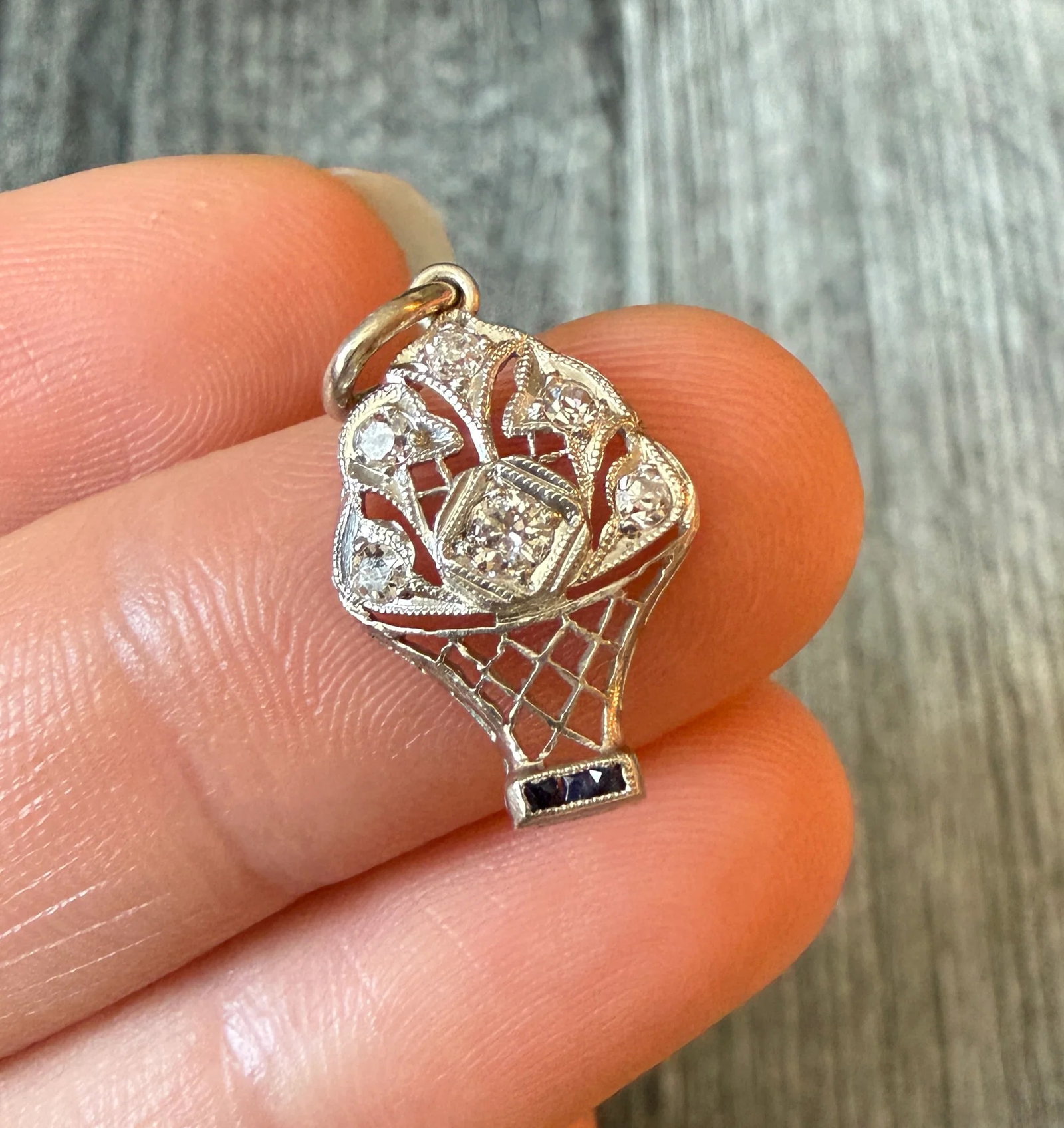 Art Deco Diamond and Sapphire Flower Basket Charm in Platinum: Metal: PlatinumWeight: 1.8 gramsDiamonds: Approximately 0.13 caratsSapphires: Approximately 0.03 caratsMeasurements: 0.65 inches long by 0.45 inches wideCondition: In very good condition with some min