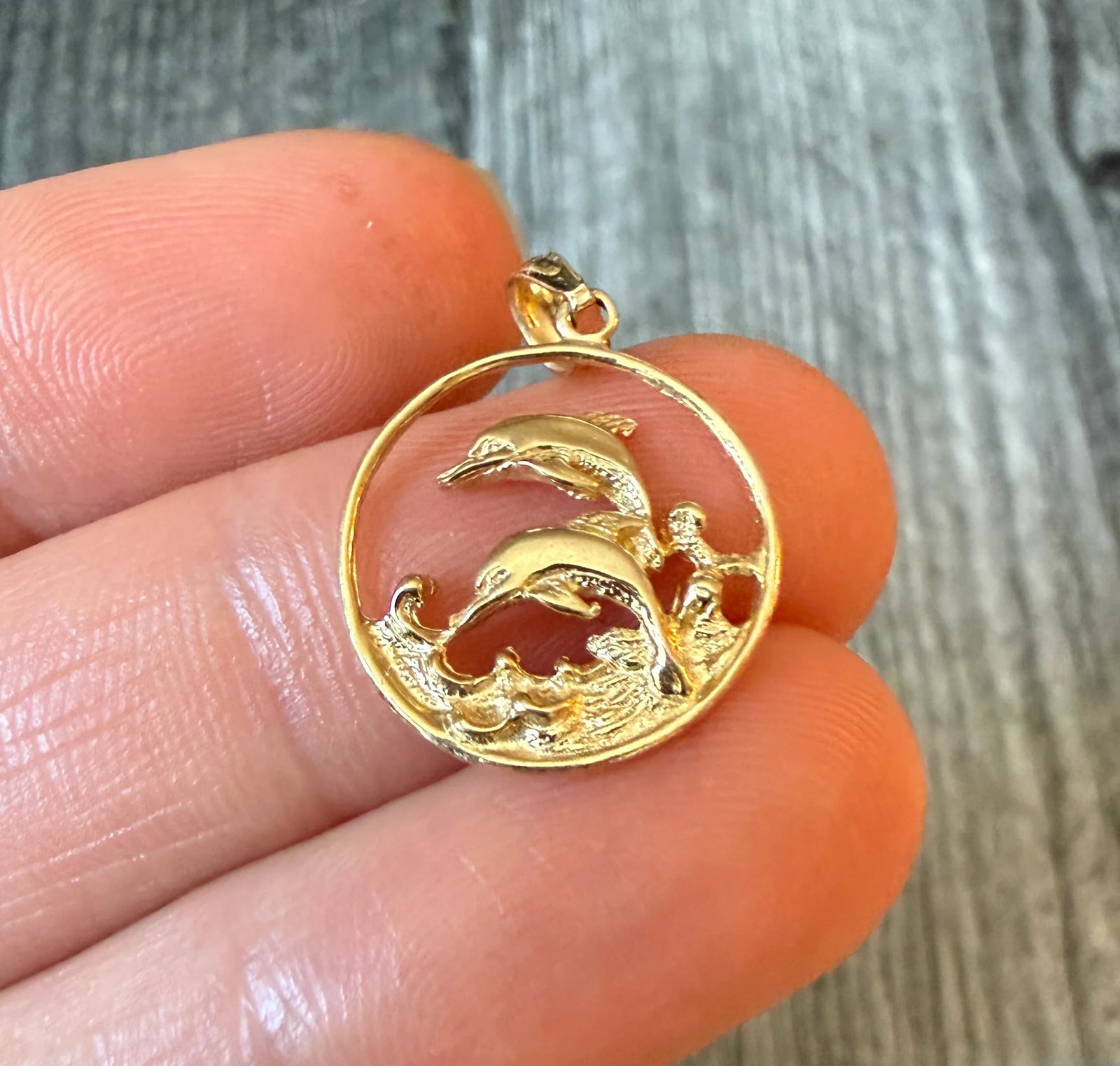 Pair of Dolphins Jumping in Water Charm in 14K Gold: Metal: 14K Yellow GoldWeight: 1.3 gramsMeasurements: 0.7 inch diameter Markings: "14K"Condition: In good condition with some minor surface wear Follow us on Instagram @alphaomegajewelry for the latest