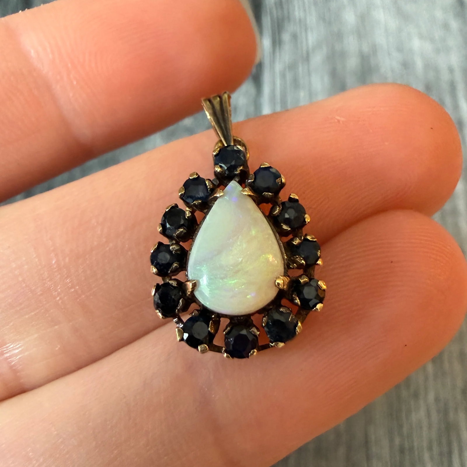 Pear Shaped Opal and Sapphire Halo Charm in 14K Gold: Metal: 14K Yellow GoldWeight: 2.6 gramsOpal: 10 mm by 7 mm by 2.7 mmSapphires: Approximately 1.12 caratsMeasurements: 0.65 inches long by 0.5 inches wideMarkings: "14K"Condition: In good condition wit