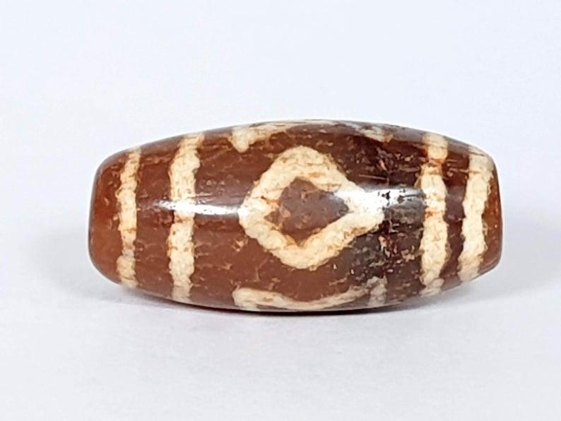 Tibetan Carnelian Dzi with Heaven & Earth Motif Variant: Dzi beads are believed to have strong powers to bring Luck, Wealth, Good Health, and Success. They also Expel Evil and Act as a Protector. The Heaven & Earth Motif is believed to bring the balance of 