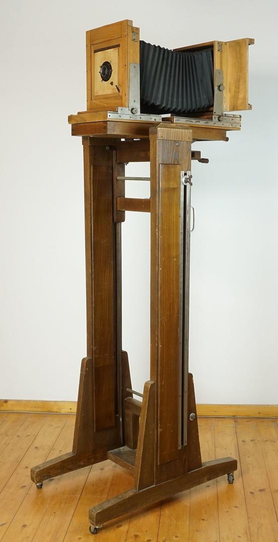 Studiobalgenkamera a 1920: Studiobalgenkamera, um 1920 Holz, Atelierkamera mit höhenverstellbarem Untergestell auf Rollen, kurbelverstellbarem Neigungswinkel. Aristostigmat-Satz Nr. 2 Objektiv von Hugo Meyer Görlitz N