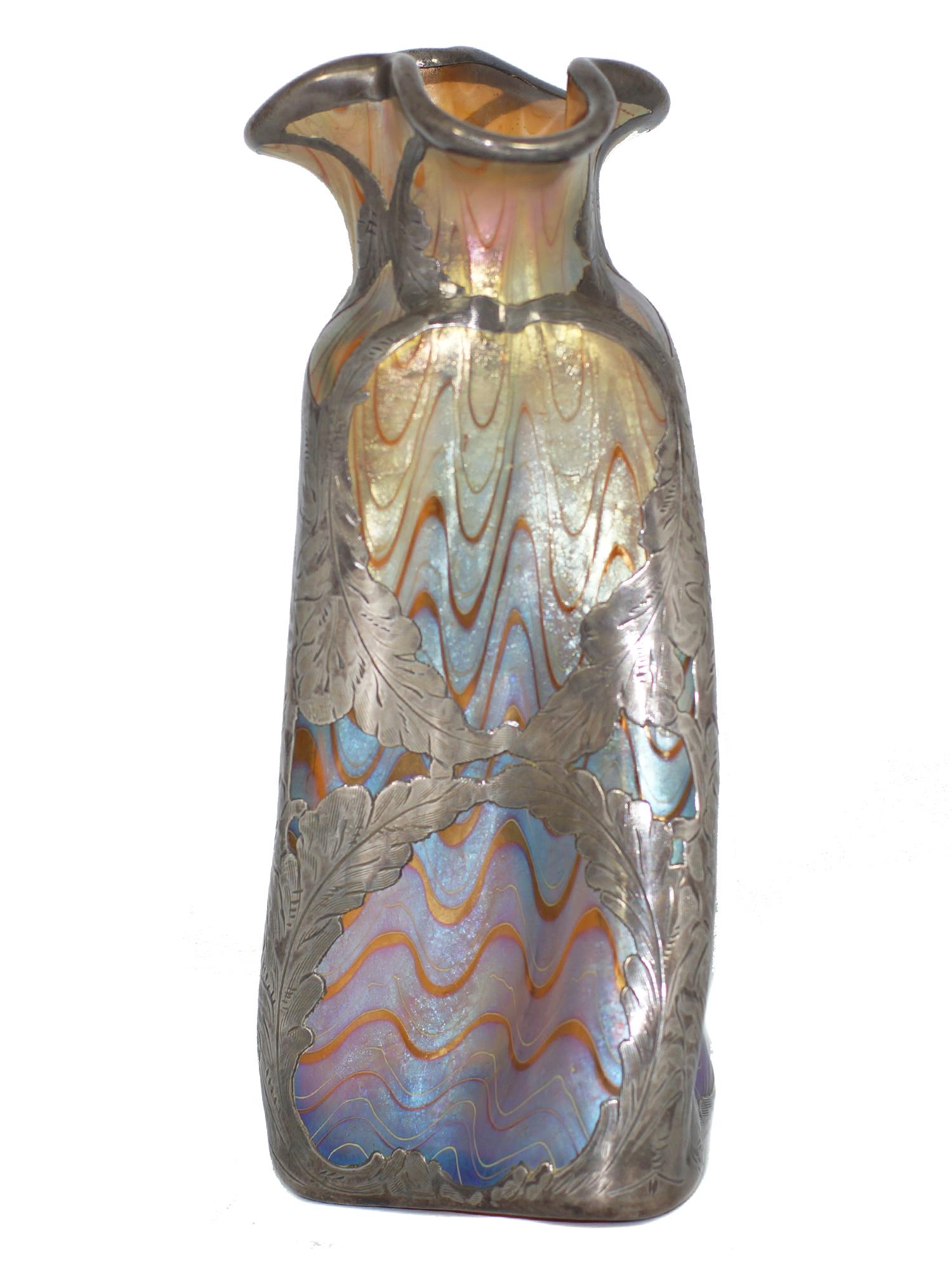 An Antique Loetz Glass Vase with Silver Overlay: A Loetz golden magenta Titania genre silver overlay Art Nouveau glass vase. The vase has a thick silver overlay with a beautiful leaf design around the shoulder of the vase. Titania was introduced in