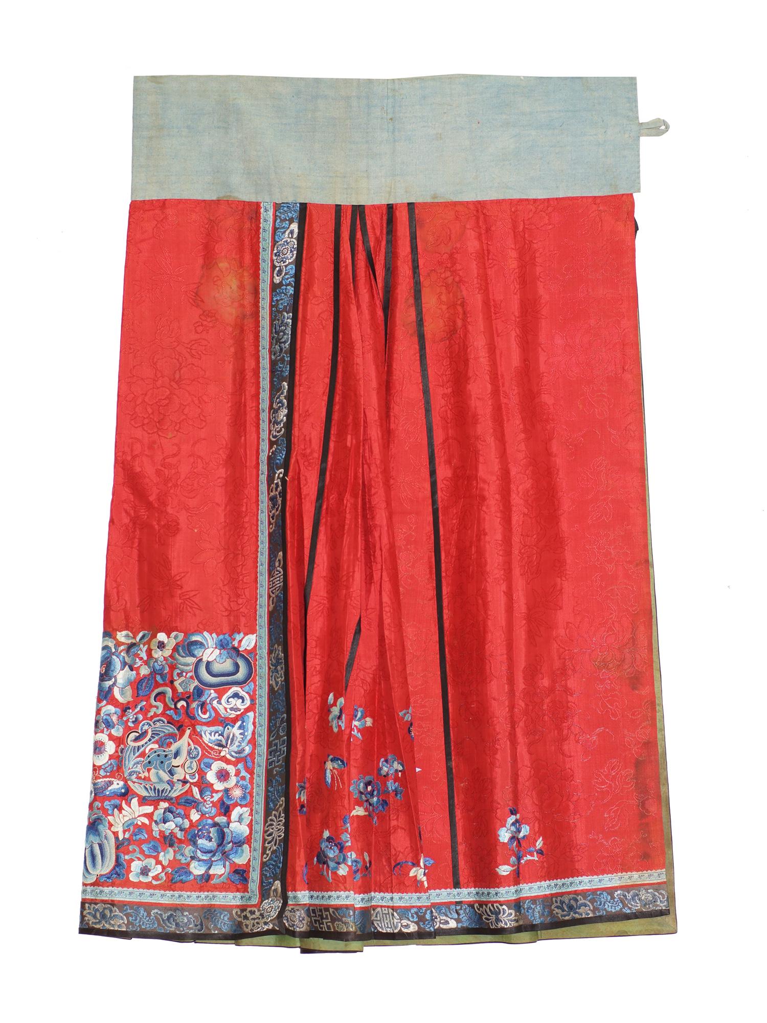 AN ANTIQUE CHINESE EMBROIDERED SILK SKIRT. LATE 19TH C.: The red silk field of the skirt is decorated with a damask floral pattern. The side embroidery is made in graceful transitions from dark blue to pure white. In the center you can see the frog, the Yin