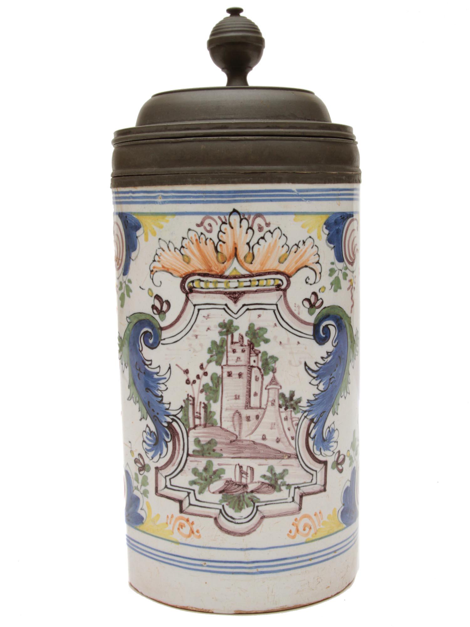 AN ANTIQUE GERMAN FAIENCE BEER STEIN 19TH C: An antique German hand painted beer stein with pewter lid and base. Decorated with colored painting depicting various curls, acanthus leaves, as well as a coat of arms with a castle on it. Unmarked. D