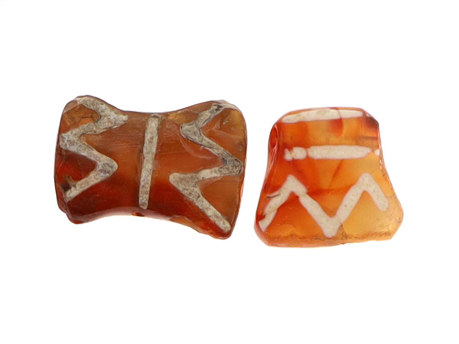 WEST ASIA ETCHED CARNELIAN BEADS. CA. 3000-2000 B.C.: Two axe-shaped etched carnelian beads. One is in a shape of a double-sided axe, while the other bead is in the shape of a one-sided axe. Dimensions: Smallest L: 3/8 in., 9 mm.Largest L: 1/2 in., 13 mm