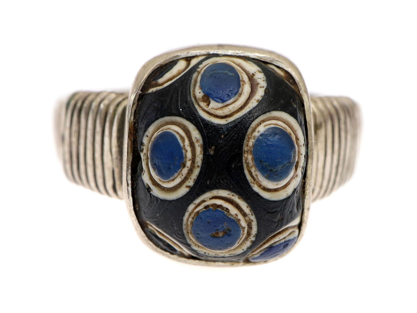 A PRE-ISLAMIC GLASS BEAD SILVER RING C.610 A.D.: Ancient Pre-Islamic broken glass blue bead with eyes on silver ring. Silver wire wrapped around the shoulder and teardrop design is at the middle of shank. Dimensions: US: 7
