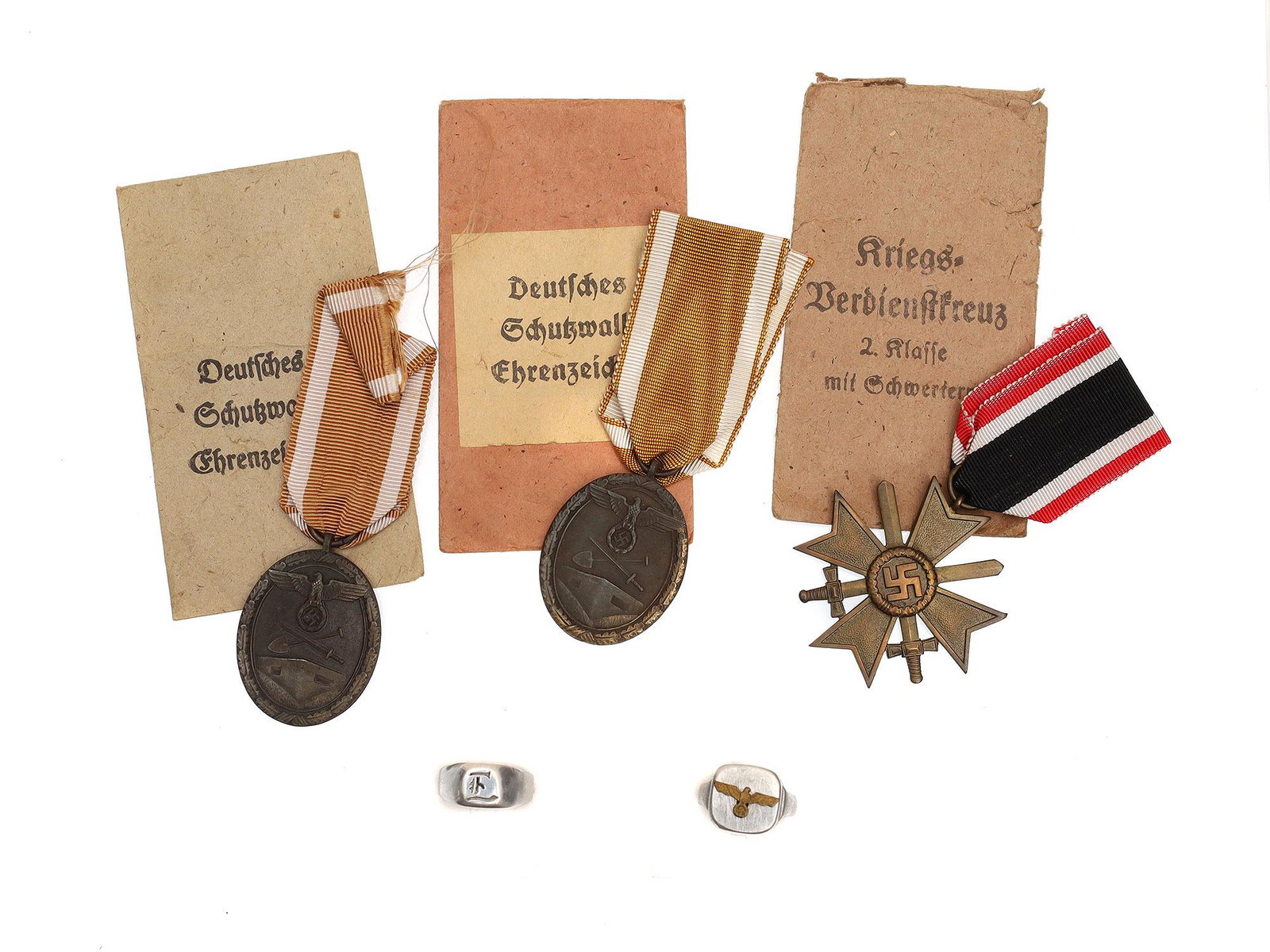 A LOT OF THREE GERMAN WWII MEDALS AND RINGS: Lot includes: 2 WWII German "West Wall" Medals, a War Merit Cross II Class, a Kriegsmarine ring, and a custom ring with a cursive German "L." Dimensions: Smallest: 1 1/4 x 1 5/8 in.Largest: 1 7/8 x 1 
