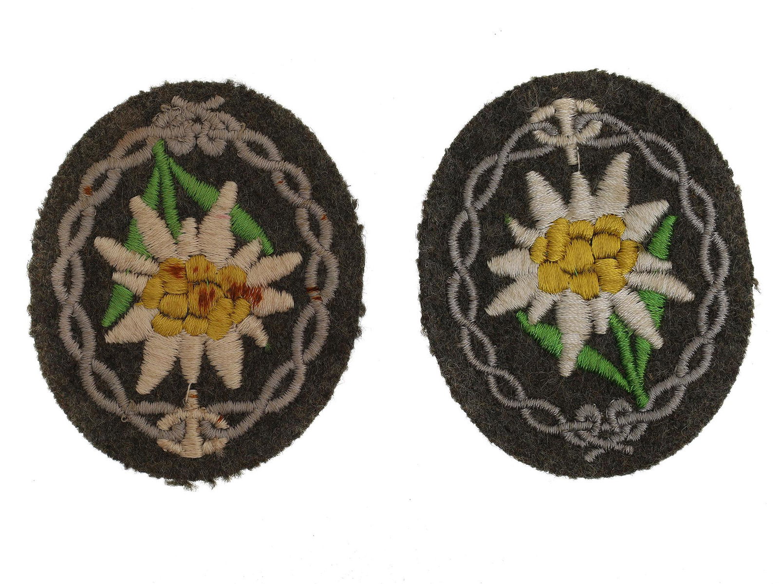 TWO WWII WEHRMACHT MOUNTAIN JAGER SLEEVE PATCHES: Original German WWII sleeve patches in the form of ovals made of black wool with machine embroidery in the form of an edelweiss flower surrounded by an ornament. Dimensions: 2 1/8 x 2 5/8 in.