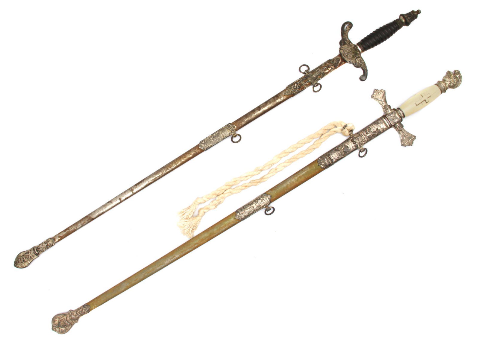 TWO MASONIC CEREMONIAL SWORDS BY OHIO COMPANIES: A pair of Masonic swords made by Prestigious Ohio based companies. The first sword featuring a black leather handle and a cross guard with an emblem and M C- K.O T.M abbreviation on the center, the ri