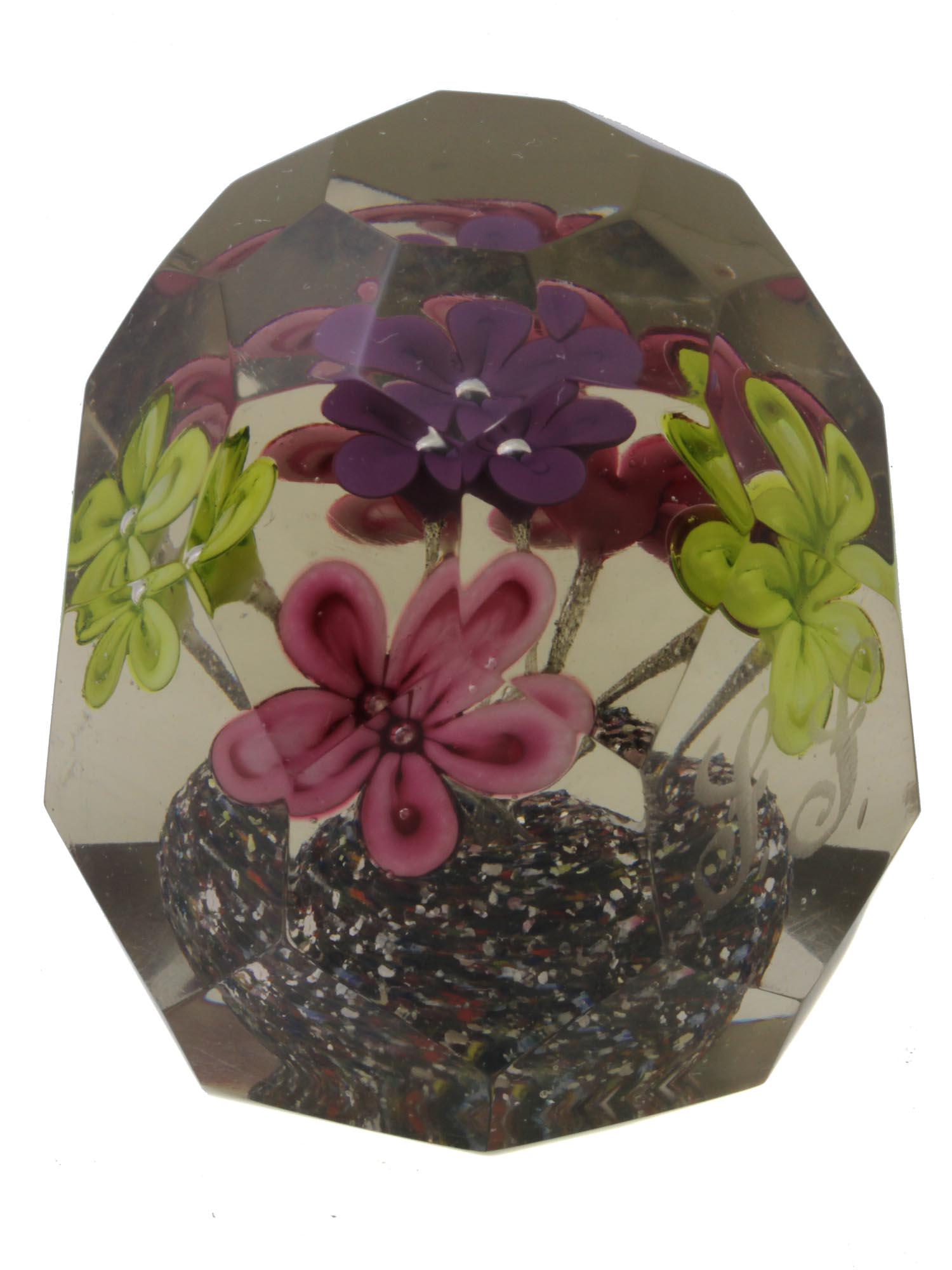 A VINTAGE SIGNED ART GLASS PAPERWEIGHT: A collectible vintage art glass paperweight, faceted shape, signed and decorated inside with two yellow, one purple, and two pink flowers. Dimensions: H: 3 3/8 in.