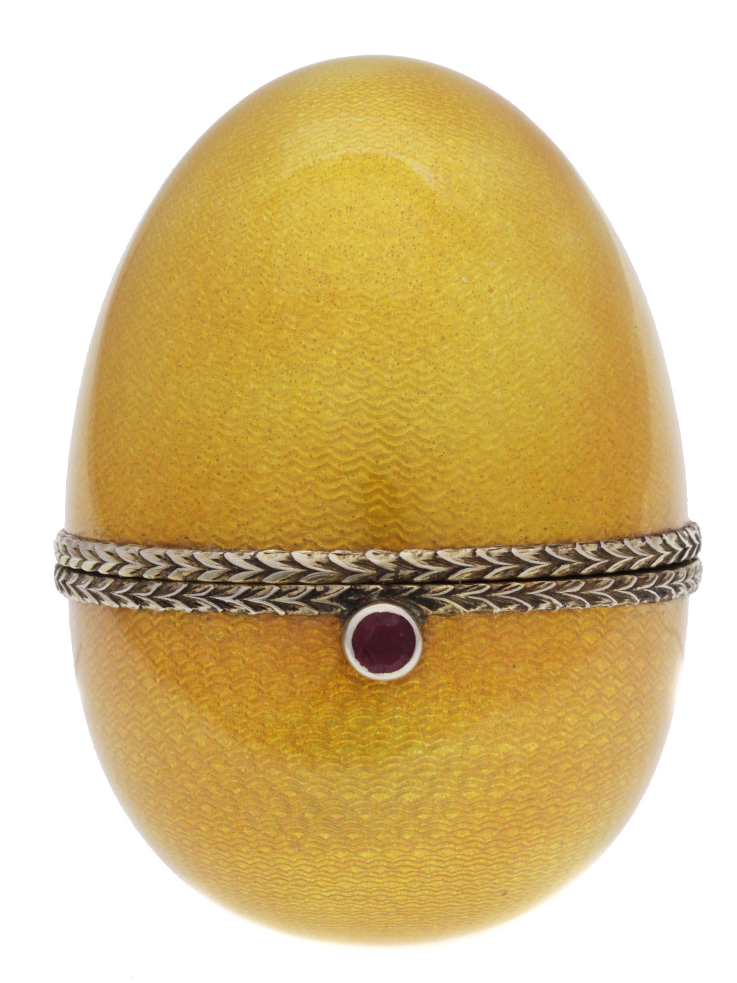 A RUSSIAN 84 SILVER GUILLOCHE ENAMEL EASTER EGG: A Russian Easter Egg, separated into two fastened halves, made of 84 silver, with an admirable exterior made of yellow-colored textured guilloche enamel with an incrusted carved ruby stone on the egg 