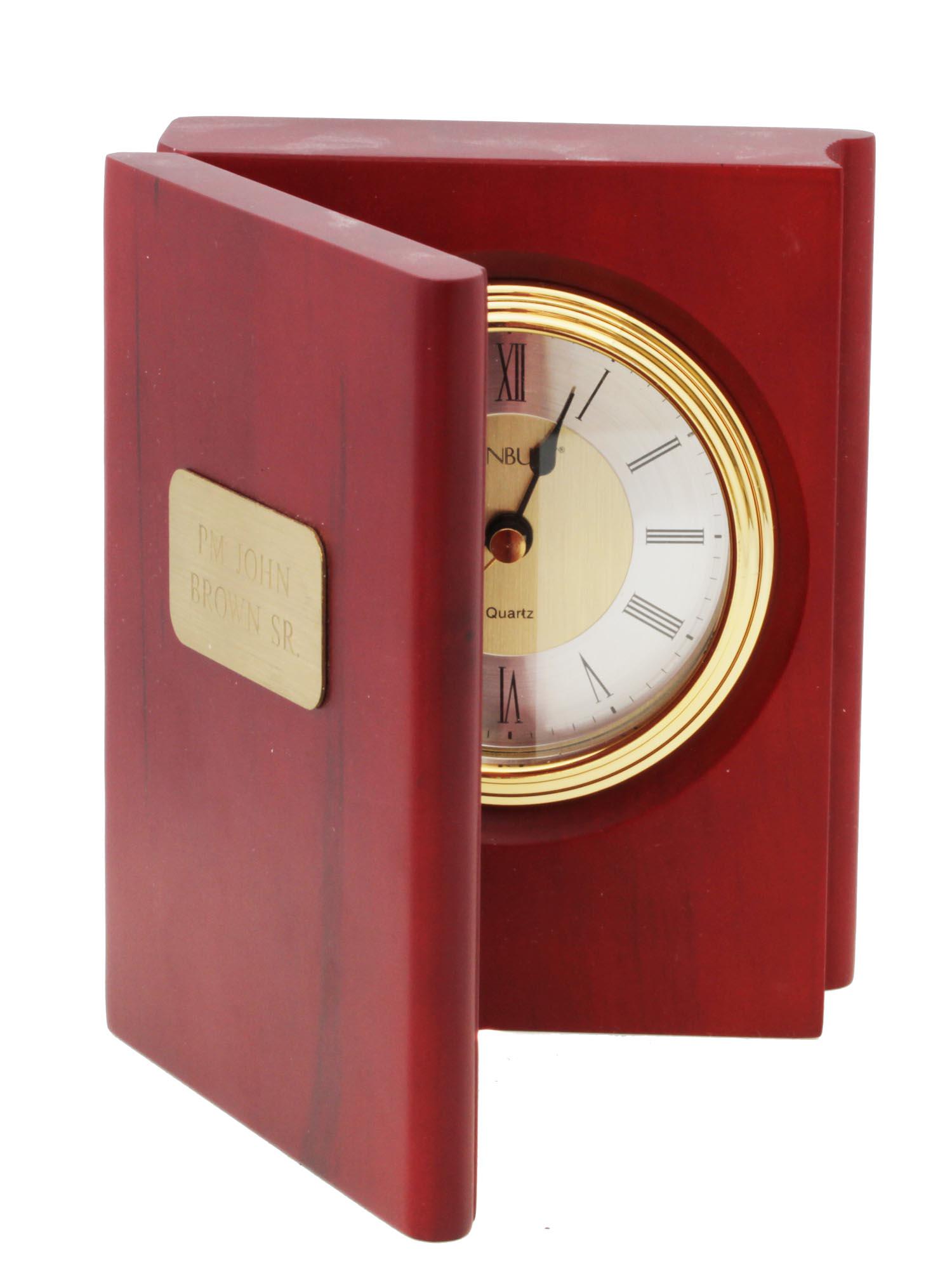 A WOOD BOOK DESK CLOCK THINGS REMEMBERED DANBURY: A personalized desk or mantel wood clock by Things Remembered made in the shape of a book, with a clock by Danbury. The exterior of the front side of the book contains a gold-colored engraved plate, i
