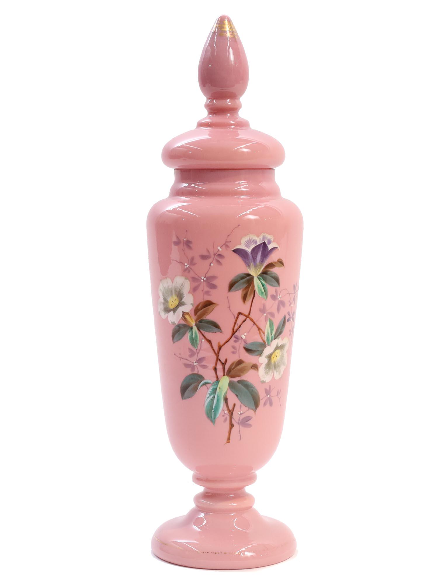AN ANTIQUE OPALINE GLASS ENAMELED VASE: A gorgeous antique tall French opaline glass vase. A light pink opaline glass jar on a pedestal with a lid, decorated with delicate enameled floral patterns depicting beautiful flowers on branches wit