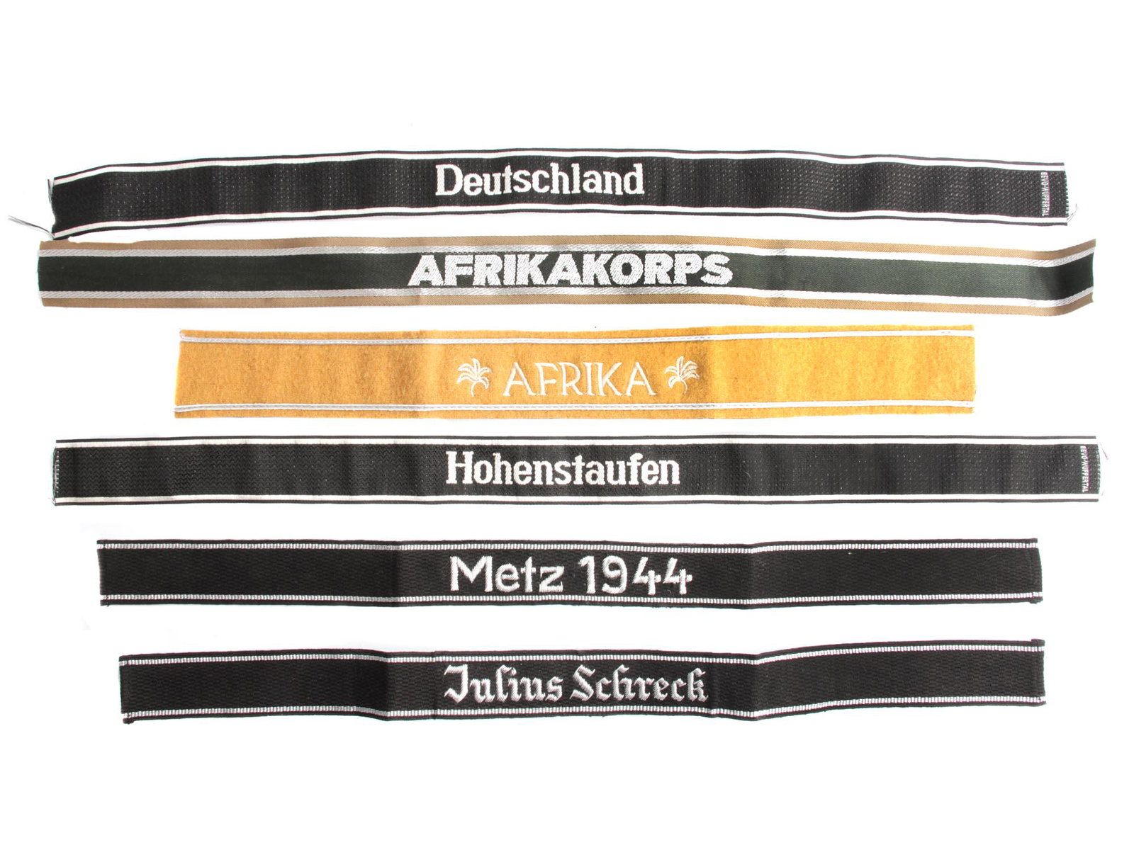 A WWII SET OF SIX GERMAN WAFFEN SS CUFF TITLES: A set of six German WWII Waffen SS Division cuff titles: "Deutschland", "Hohenstaufen", "Julius Schreck", "Africa Corps", "Africa", "Metz 1944". Five of the cuff titles are black with silver and white