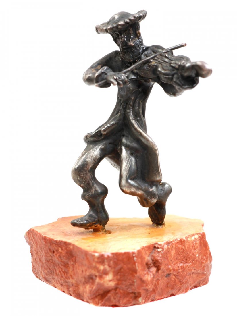 A SILVER JUDAICA SCULPTURE OF VIOLIN PLAYER: A silver sculpture depicting a violin player in a hat. The sculpture is mounted on a stone base. A red velvet lining on the bottom. Dimensions: H: 3 1/2 in.
