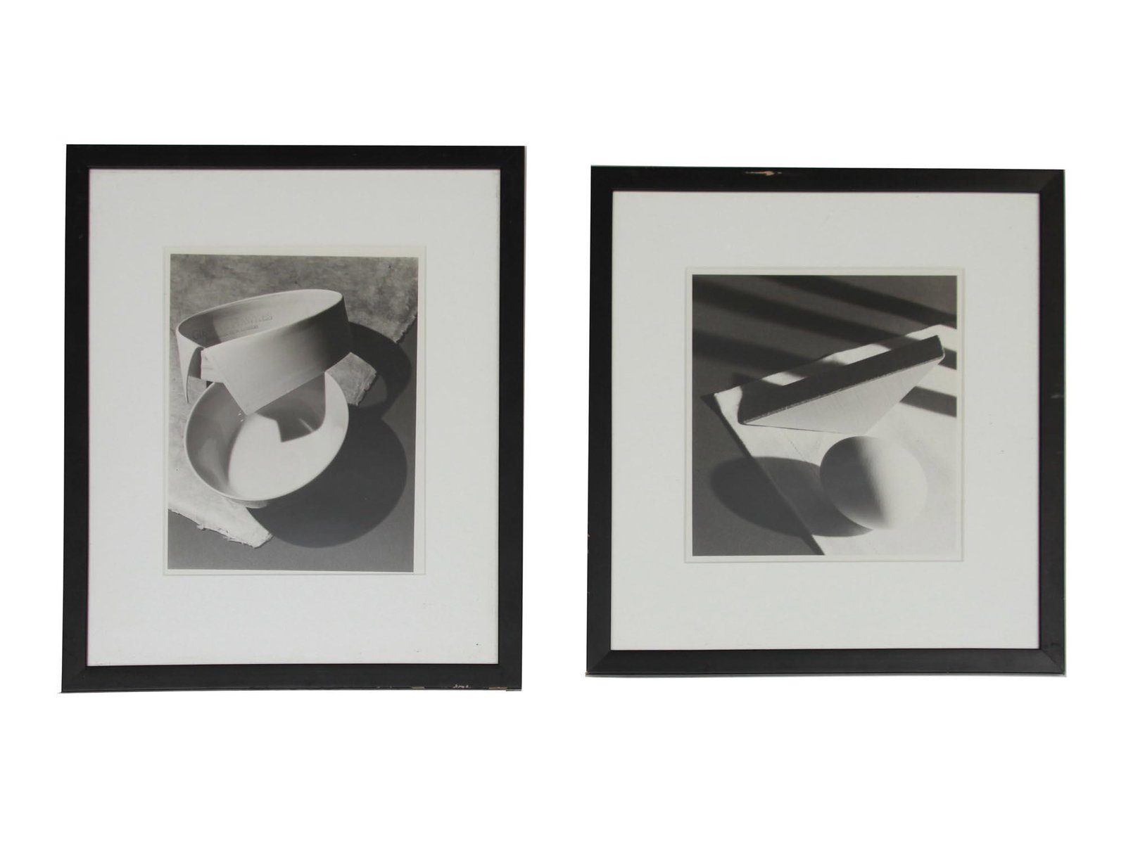 A PAIR OF STILL LIFE BLACK AND WHITE PHOTOGRAPHS: A pair of still-life black and white photographs. The first depicts a white gentleman collar and round plate. The second depicts a chicken egg, triangular object and falling shadows. Both framed. Dime