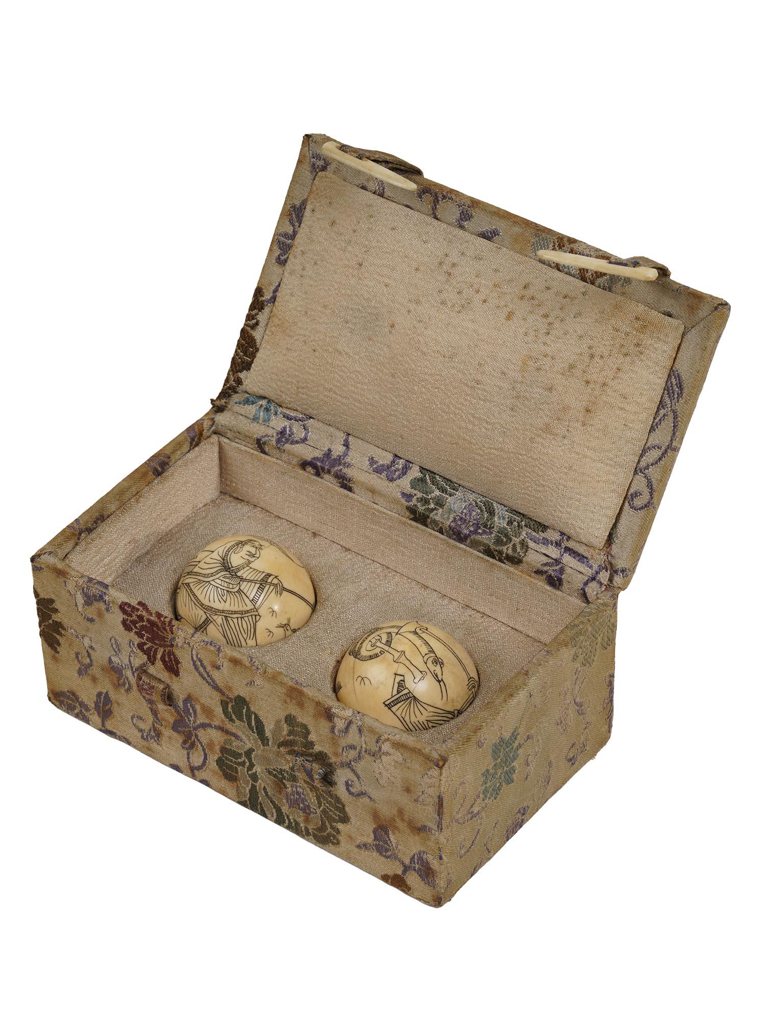 A PAIR OF JAPANESE HAND CARVED NETSUKE BALLS: A pair of Japanese hand carved from natural materials and stained netsuke balls adorned with traditional images of animal charmers in traditional costumes. Completed with an original upholstered box w