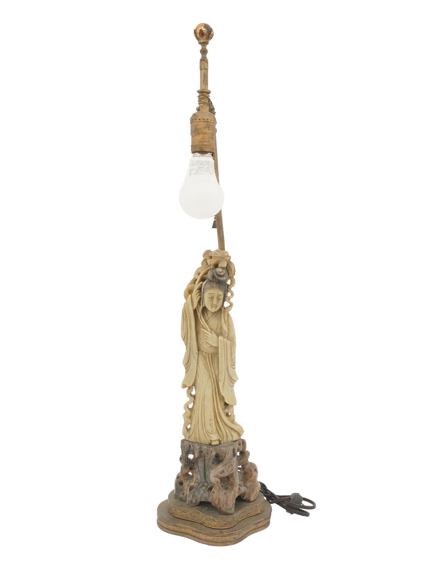ANTIQUE CHINESE CARVED SOAPSTONE FIGURAL TABLE LAMP: An antique oriental converted to an electrical table lamp with a single light fixture. The base and shaft of the lamp are made of brass with ornamental metalwork. A hand-carved and painted soapstone f