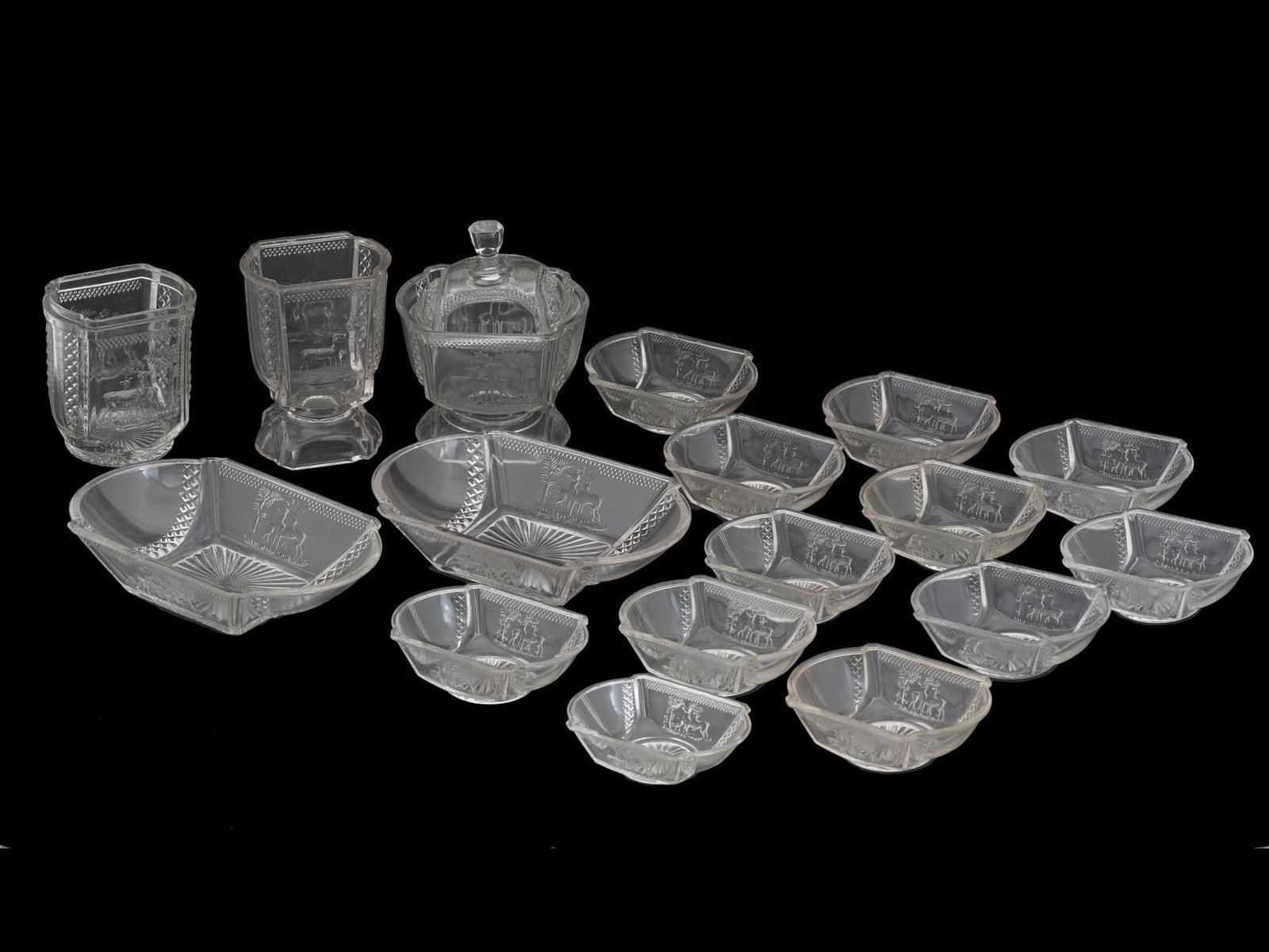 ANTIQUE MCKEE EAPG DEER AND PINE TREES GLASS SET: A collection of antique 1883 original American McKee and Brothers EAPG pressed glass table wares. The collection includes twelve dessert bowls, pair of dishes, one covered and footed candy bowl, pair 