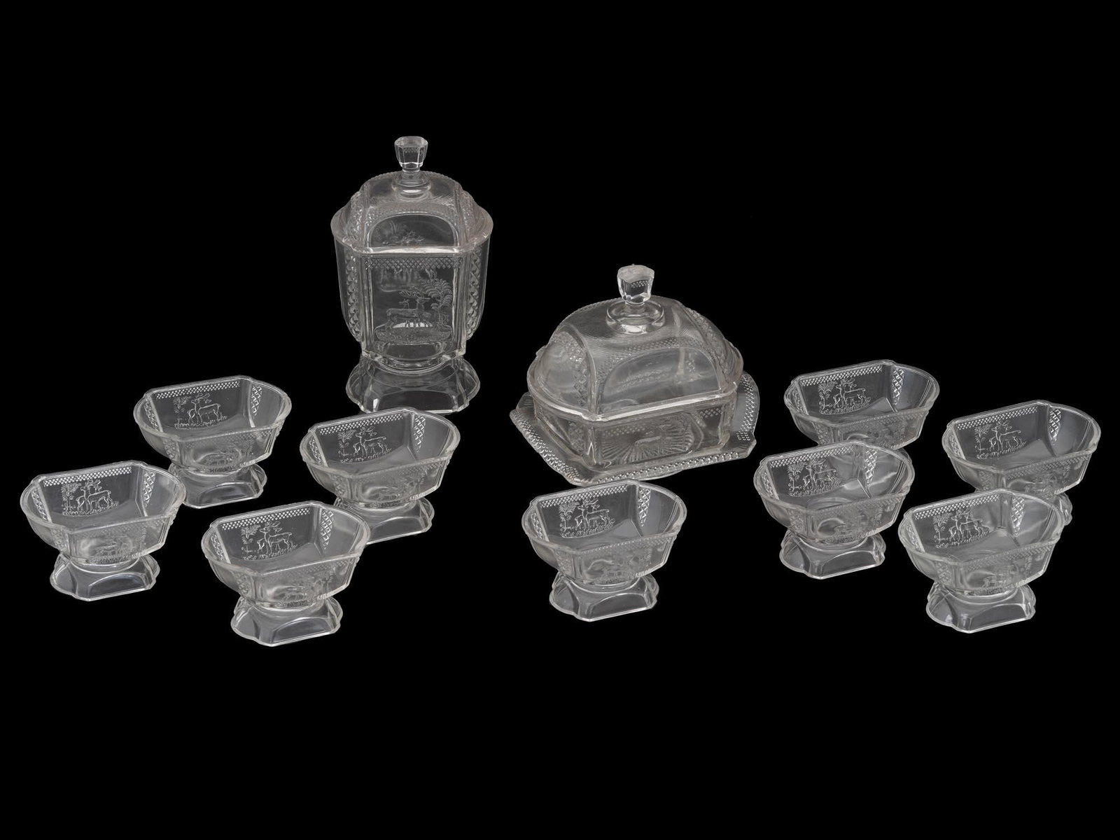 ANTIQUE MCKEE EAPG DEER AND PINE TREES GLASS SET: A collection of antique 1883 original American McKee and Brothers EAPG pressed glass table wares. The collection includes nine footed dessert bowls, one covered butter dish, and one covered candy bowl