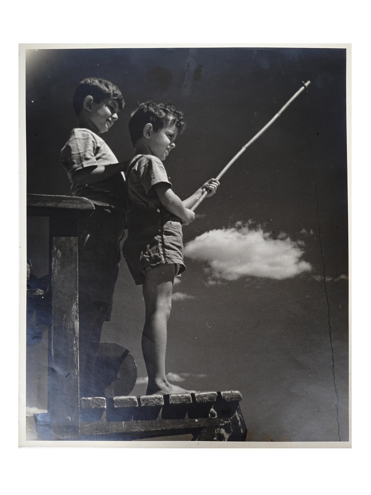 1940S AMERICAN PHOTOGRAPH BY NATHANIEL FIELD: A mid century black and white photograph depicting two little boys with a fishing rod. Unsigned. Nathaniel Field was an American photographer based in Brooklyn, NY. Most of his work dates back to the 